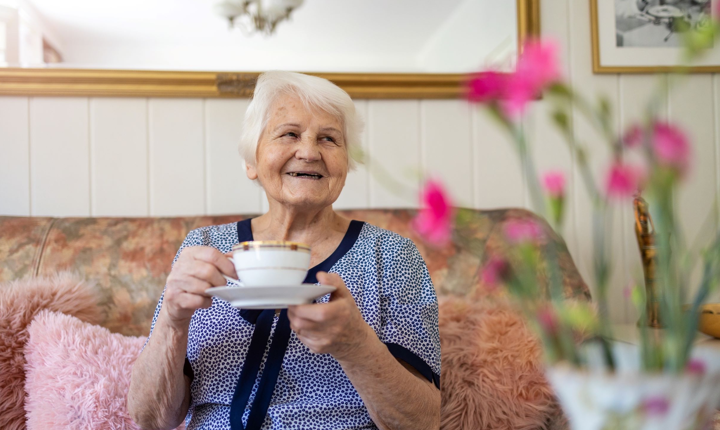 Older lady drinking tea sitting on a sofa and smiling