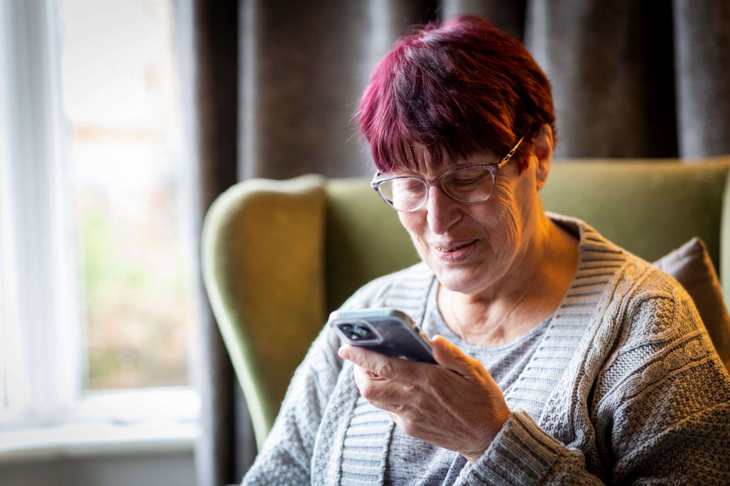 Lady using her phone sitting in an armchair